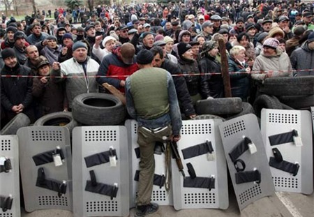 [Caption]ro-Russians shout slogans as an armed pro-Russian activist guards a police station in the eastern Ukrainian city of Slavyansk after it was seized by a few dozen gunmen on April 12, 2014. A few dozen gunmen seized a police station in Ukraine's restive eastern industrial heartland amid spreading protests in favour of the heavily Russified region joining Kremlin rule.