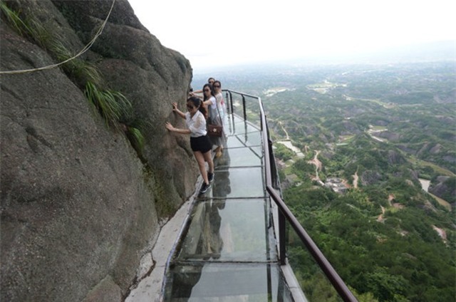 Du khách di chuyển trên sàn thủy tinh phát ra âm thanh hòa nhịp với tiếng chân bước tại khu du lịch Shiniuzhai ở Nhạc Dương, tỉnh Hồ Nam, Trung Quốc, hôm 27/5. Sàn thủy tinh được thiết kế uốn lượn theo vách đá có độ cao 300 m.