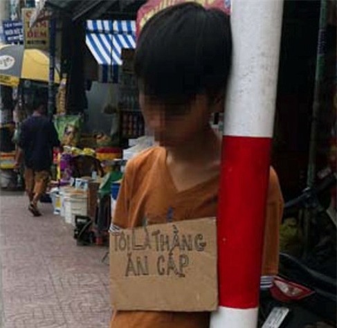 Cậu bé này trộm cắp xe để chơi game nên bị chú phạt đeo bảng “tôi là thằng ăn cắp”