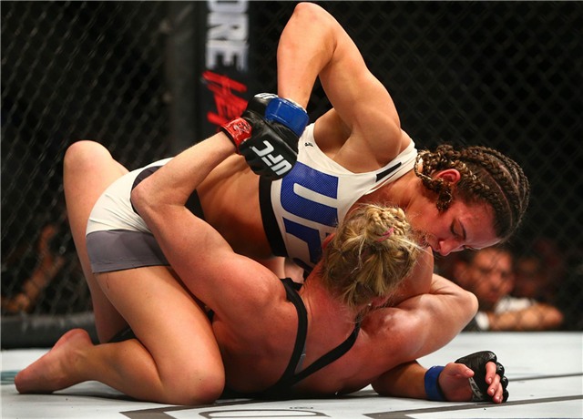 Ở trận bảo vệ đai vô địch hạng gà, Holly Holm nhập cuộc khá tự tin. Cô chủ động áp sát Miesha Tate và tung ra cú đấm vào mặt, sau đó thực hiện cú đá tầm trung chính xác vào đối phương.