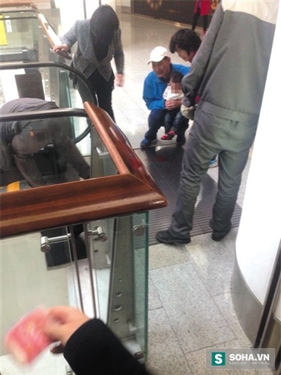 Bé gái ngồi trong lòng ông nội, hoang mang sợ hãi sau sự cố kinh hoàng. Máu từ hai bàn tay bị thương nhỏ đầy trên sàn.