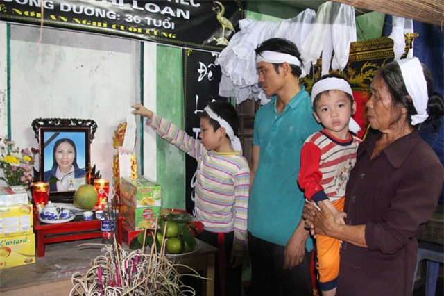 Hai bé Nguyễn Đình Quyết, 9 tuổi, học lớp 3 và bé Nguyễn Đình Huy, 4 tuổi- đầu chít khăn tang cùng bà nội và bố đứng bên bàn thờ của người mẹ thân thương.