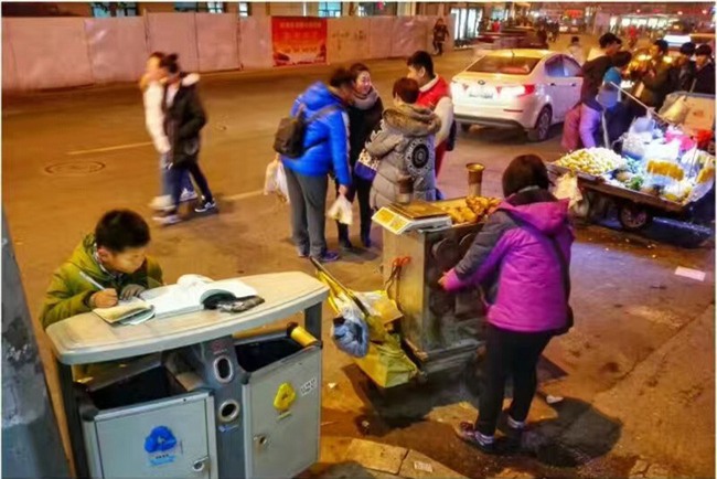 Hình ảnh cậu bé chăm chỉ học bài trên thùng rác cạnh xe khoai lang nướng của mẹ gây xúc động mạnh - Ảnh 1.