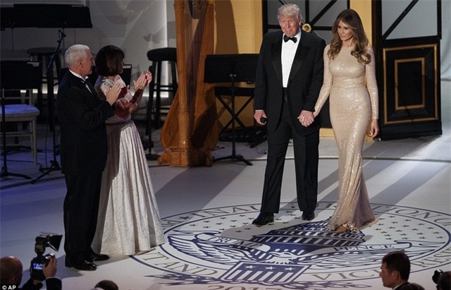 Phu nhân của ông Trump, bà Melania, với tông màu trang điểm nhẹ, xuất hiện trong bữa tiệc với một chiếc đầm đuôi cá óng ánh của nhà thiết kế nổi tiếng Reem Arca thay vì chiếc đầm của nhà thiết kế Ralph Lauren như đồn đoán trước đó. Bà sánh vai bên chồng bước ra sân khấu giữa những tràng pháo tay của hơn 1.000 khách mời. (Ảnh: AP)