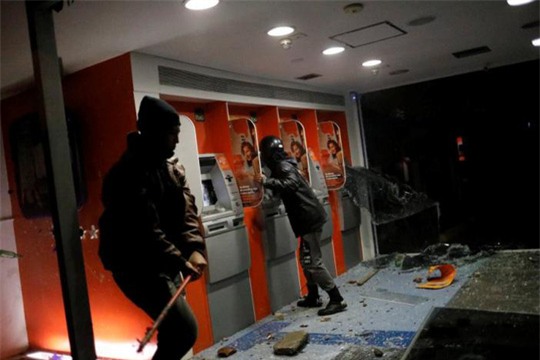 
Người biểu tình đập phá ATM. Ảnh: Reuters
