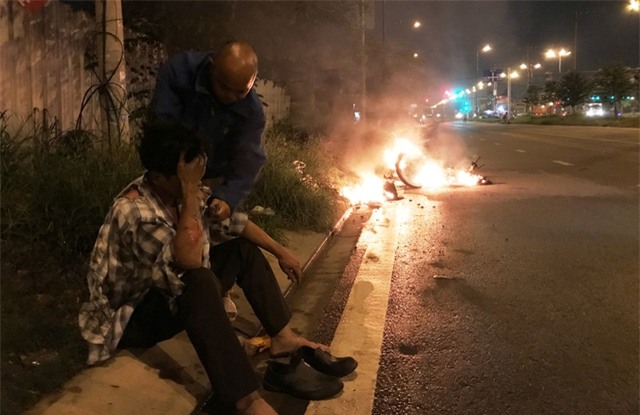 Người đàn ông (ngồi) được tài xế xe đầu kéo container giải cứu bên chiếc xe máy bao trùm trong biển lửa.