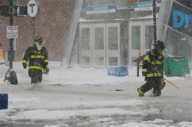 Hiện tượng tuyết rơi dày đã ảnh hưởng tới cuộc sống của hàng triệu người dân Mỹ. Các nhà chức trách và người dân ở khu vực bờ Đông nước Mỹ đang nỗ lực dọn tuyết để mở đường cho xe đi lại. Trong ảnh: Lính cứu hỏa bước qua con đường ngập trong nước và tuyết ở Boston. (Ảnh: Reuters)