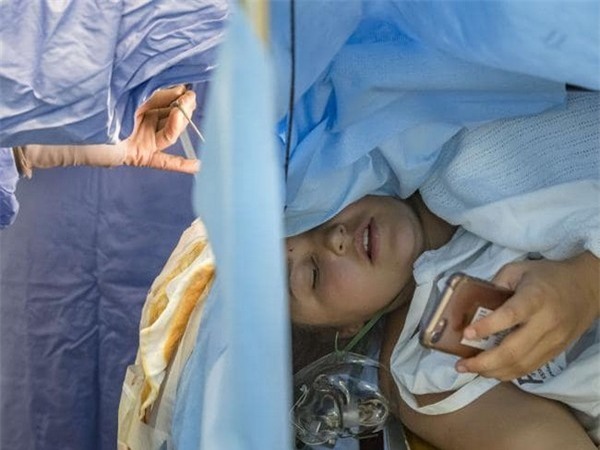 Jess Banik đang sử dụng điện thoại trong khi các bác sĩ đang tiến hành ca phẫu thuật não cho cô