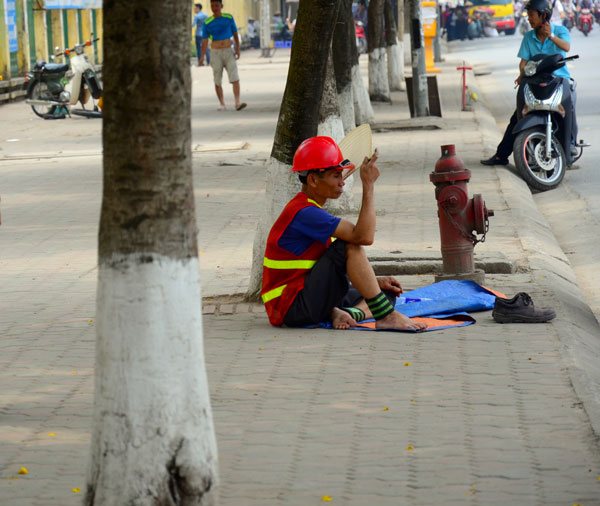 Người công nhân ngồi nghỉ trưa dưới bóng cây với chiếc quạt nan.