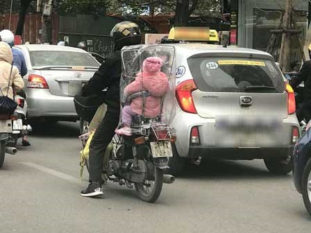 Giữa một sớm mai rét mướt, bức ảnh bé con ngồi sau xe bố trùm kín nilon khiếm lòng ta ấm áp