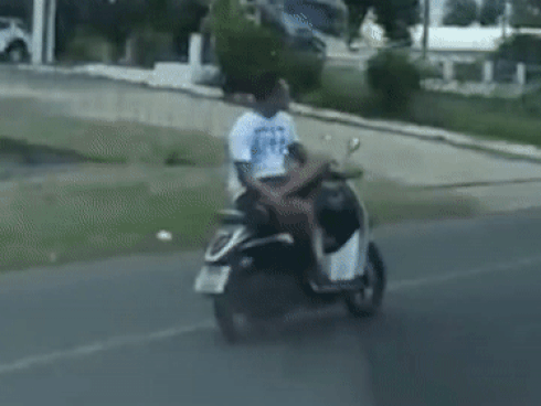 Quái xế ngồi vắt chéo chân lái xe máy bằng một tay