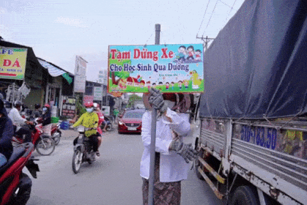Cụ bà cầm bảng điều phối giao thông để học sinh qua đường ở TP.HCM